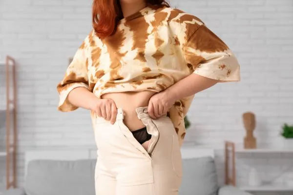Image of woman trying to do her trousers up after pregnancy weight gain Bedfordshire